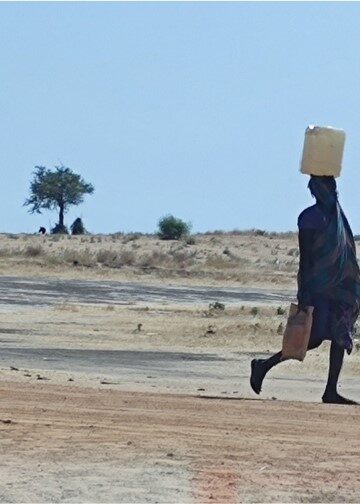 Dos personas llevando agua en el campo de refugiados Um Sangour en Sudán