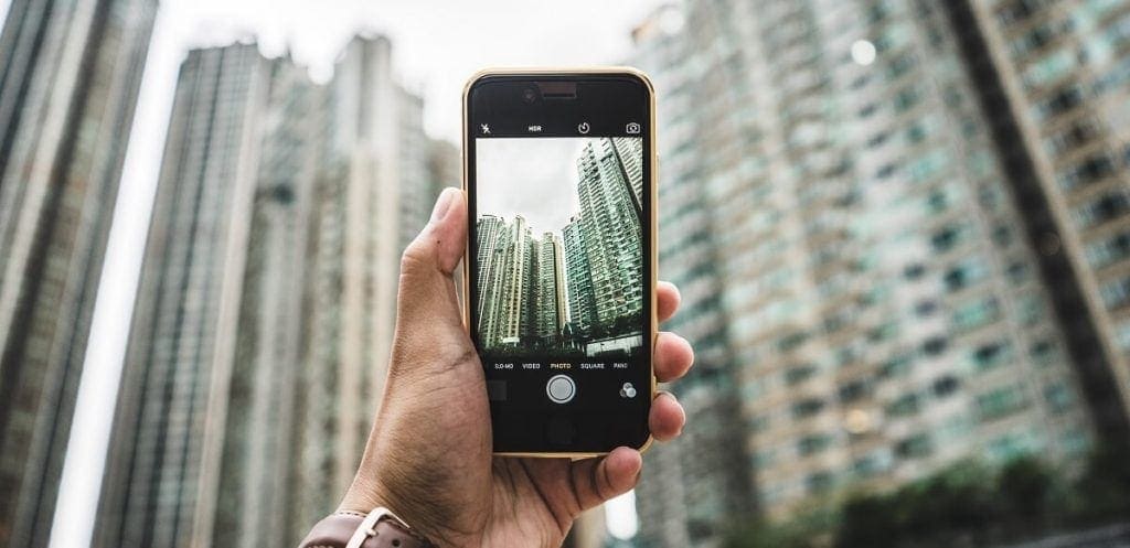 Someone holds a mobile phone in selfie mode, you see the landscape of a city