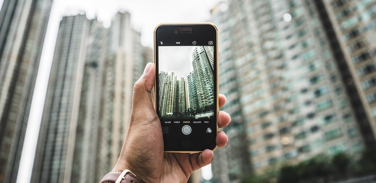 Someone holds a mobile phone in selfie mode, you see the landscape of a city
