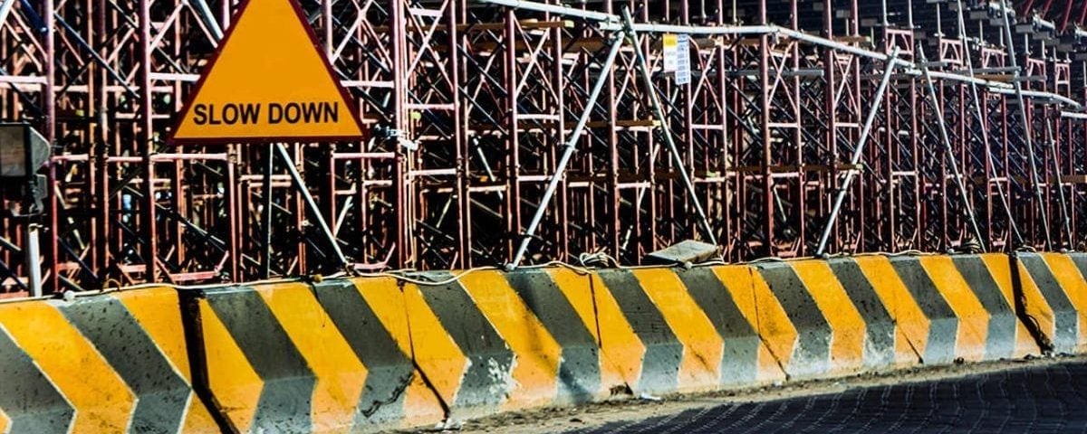 Foto de barreras pintadas en amarillo y negro para avisar de una obra, colocado delante de andamios y una señal