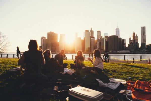 Photo of a group of people sitting on the grass of a park with a city in the background