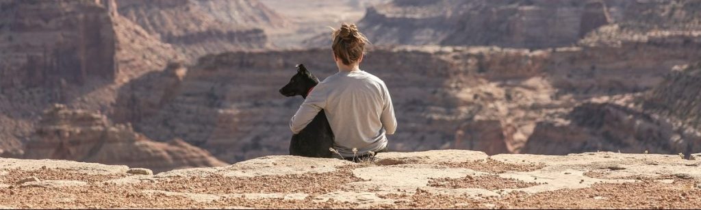 Chica con mascota de espaldas mirando desde un acantilado