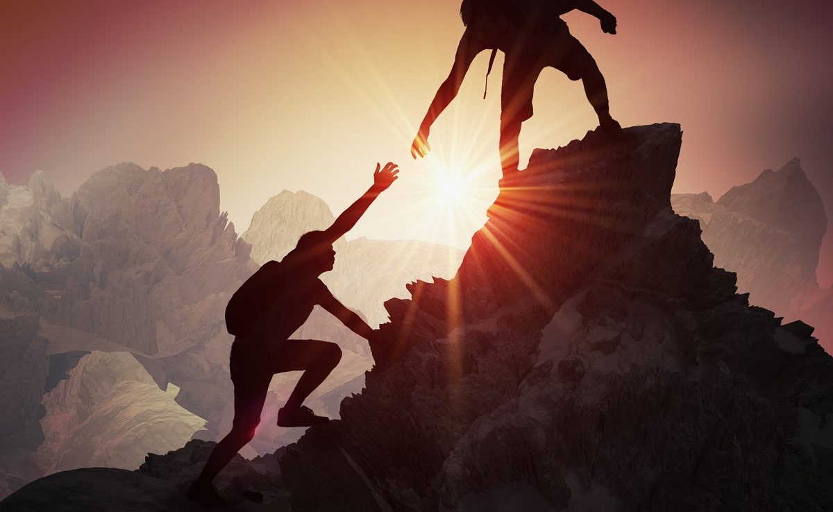 Silhouettes of two people climbing on mountain and helping.
