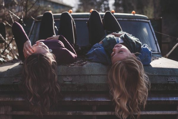 Two girls talking while lying on a car.