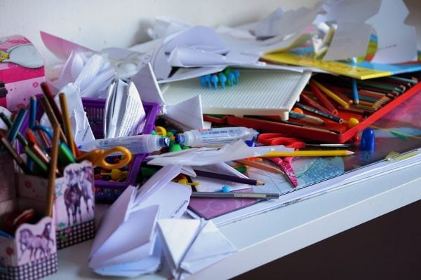 A cluttered office table with papers, scissors, crayons, etc.