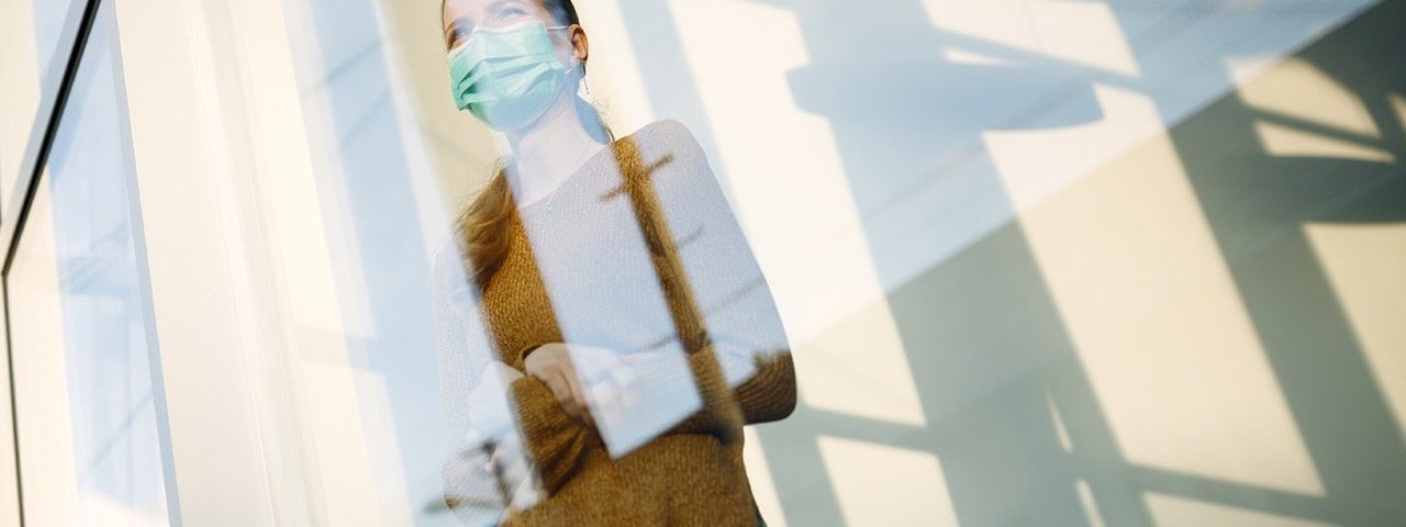 woman with face mask standing by the window