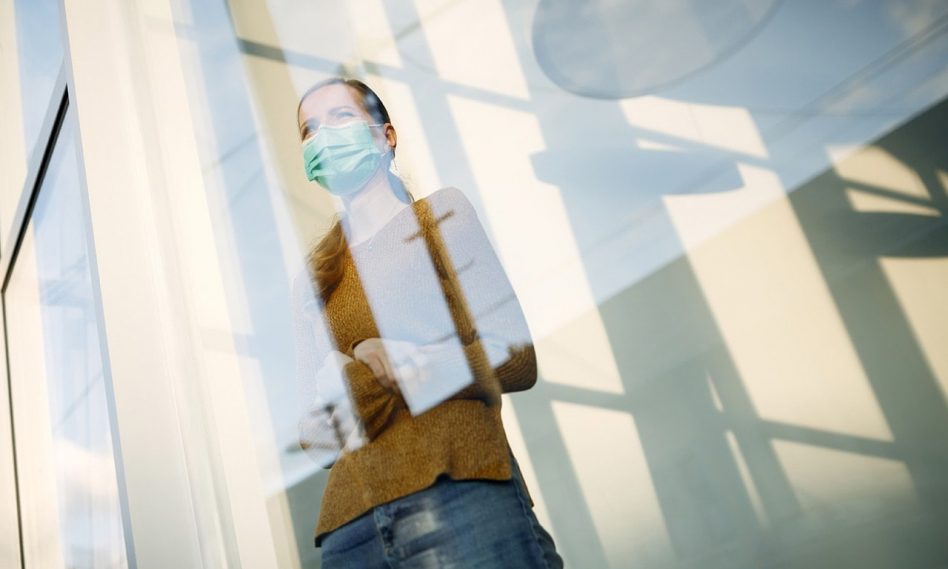 woman with face mask standing by the window