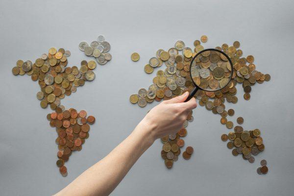 A map of the world made by coins and a hand holding a magnifying glass