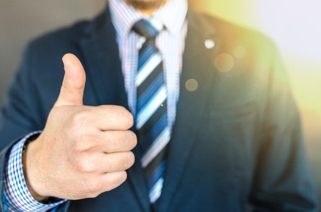 A man in a business suit showing thumbs up.
