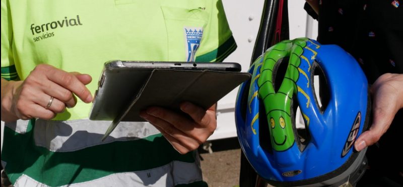 Foto de una persona con un casco de bici en la mano y un empleado de Ferrovial Servicios tomando nota en una tablet